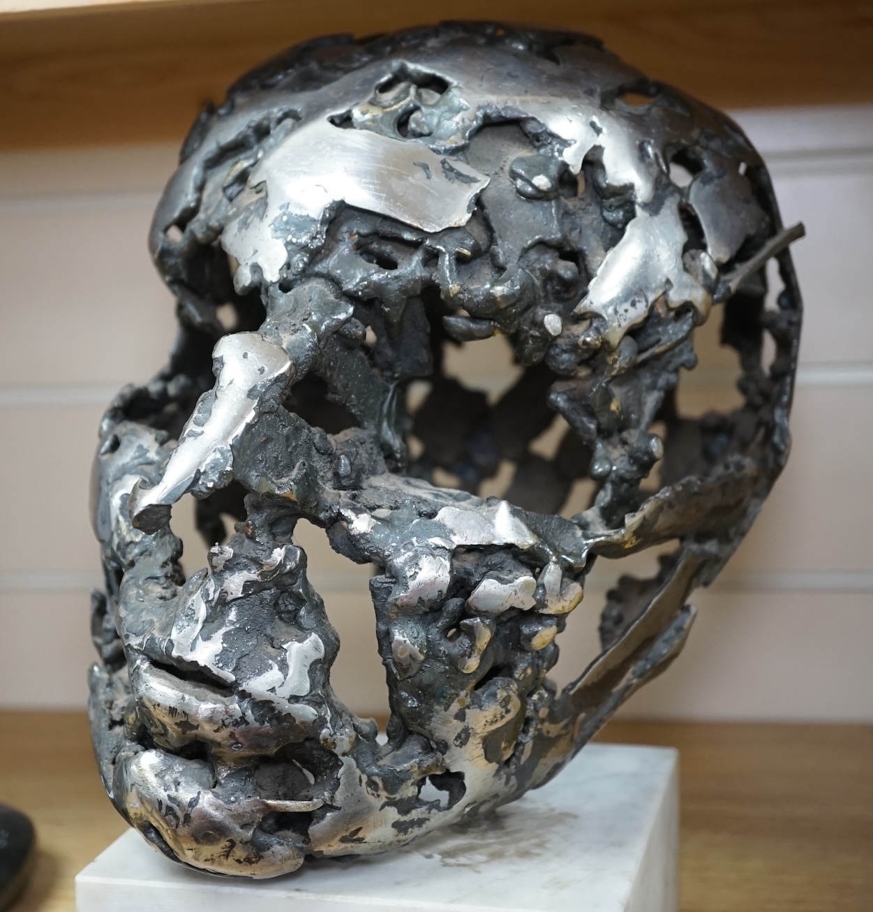 A modern polished steel skull, pierced and mounted on square white marble plinth, circa 1975, 31cm high. Condition - good, minor chipping